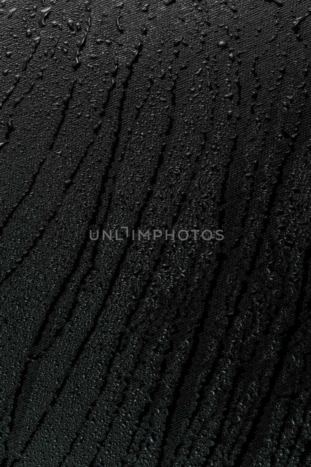 water drops on flat black rubber surface dark macro background with long smudges in vertical orientation