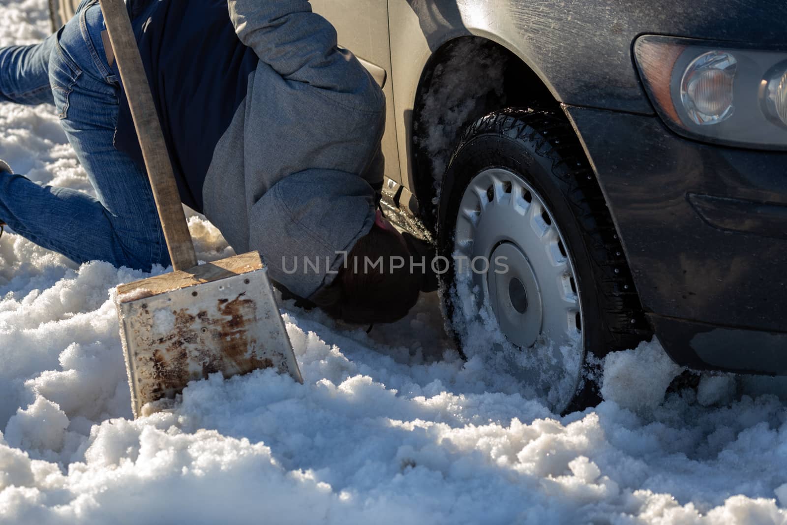 man working at car stuck in snow on knee with shovel at daylight offroad by z1b