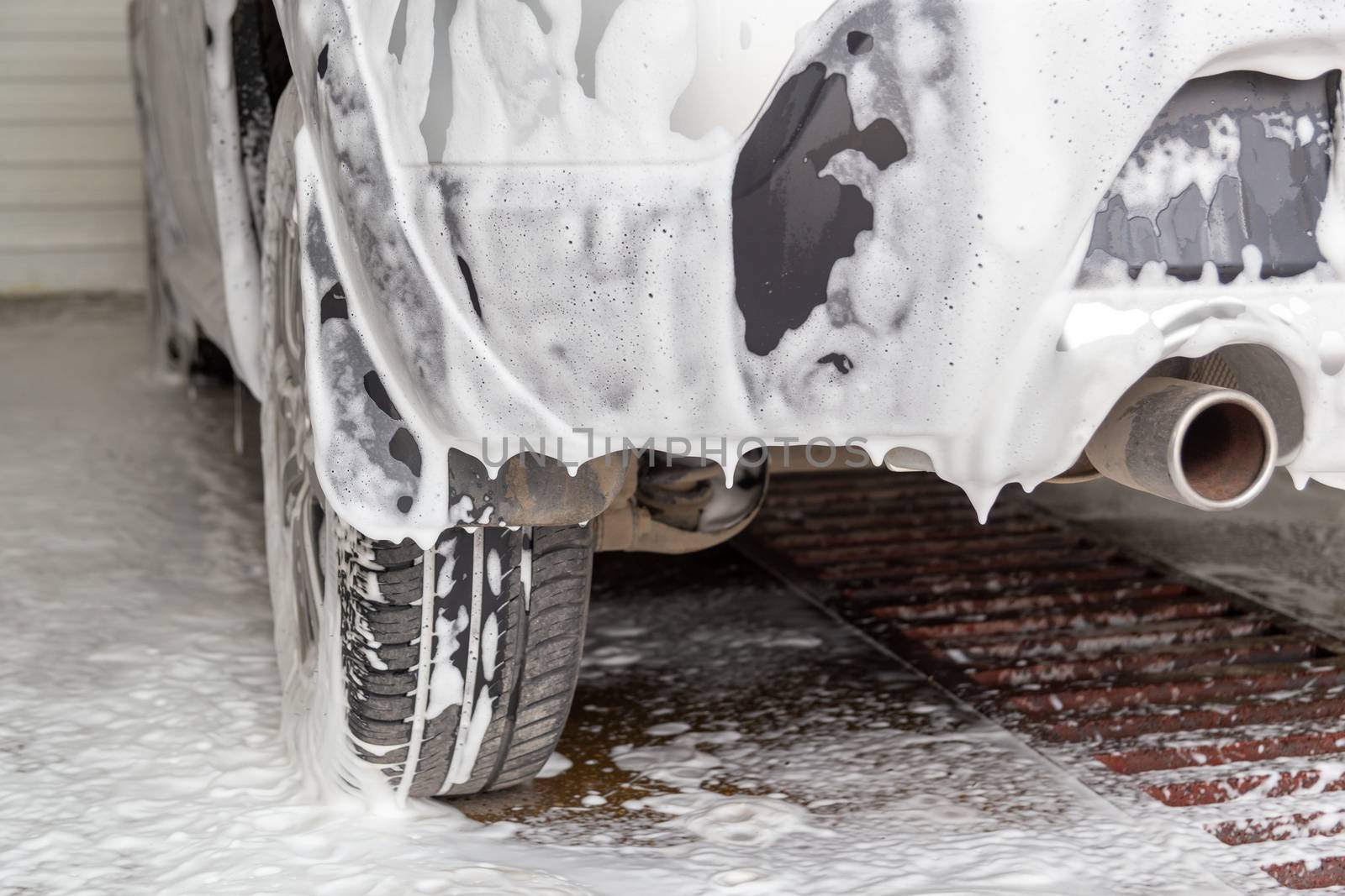 a fossil fuel car covered by soap foam while washing indoors - close-up low angle view from back with selective focus.