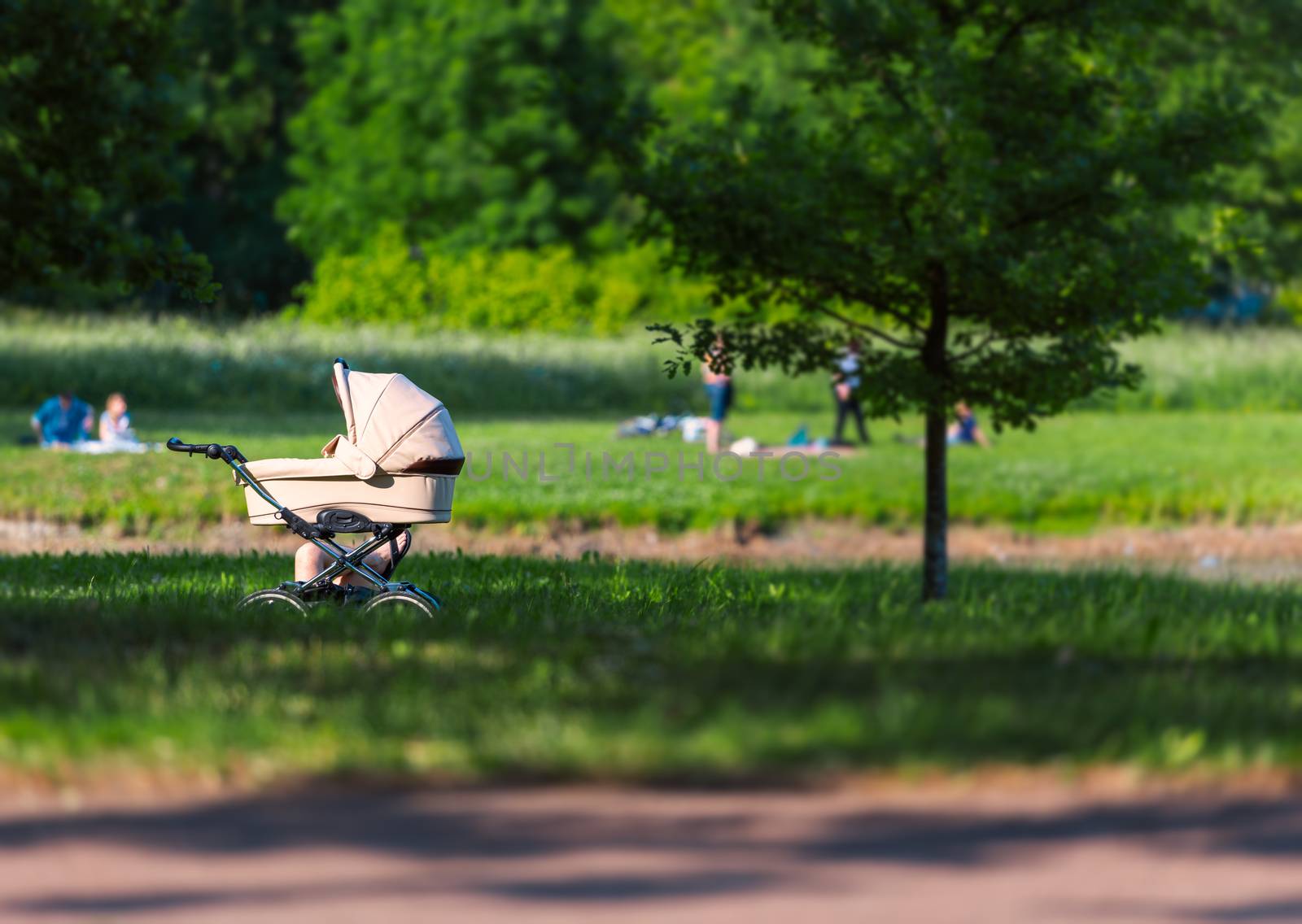 Baby carriage in park with parent nearby. People relax in city green zone.