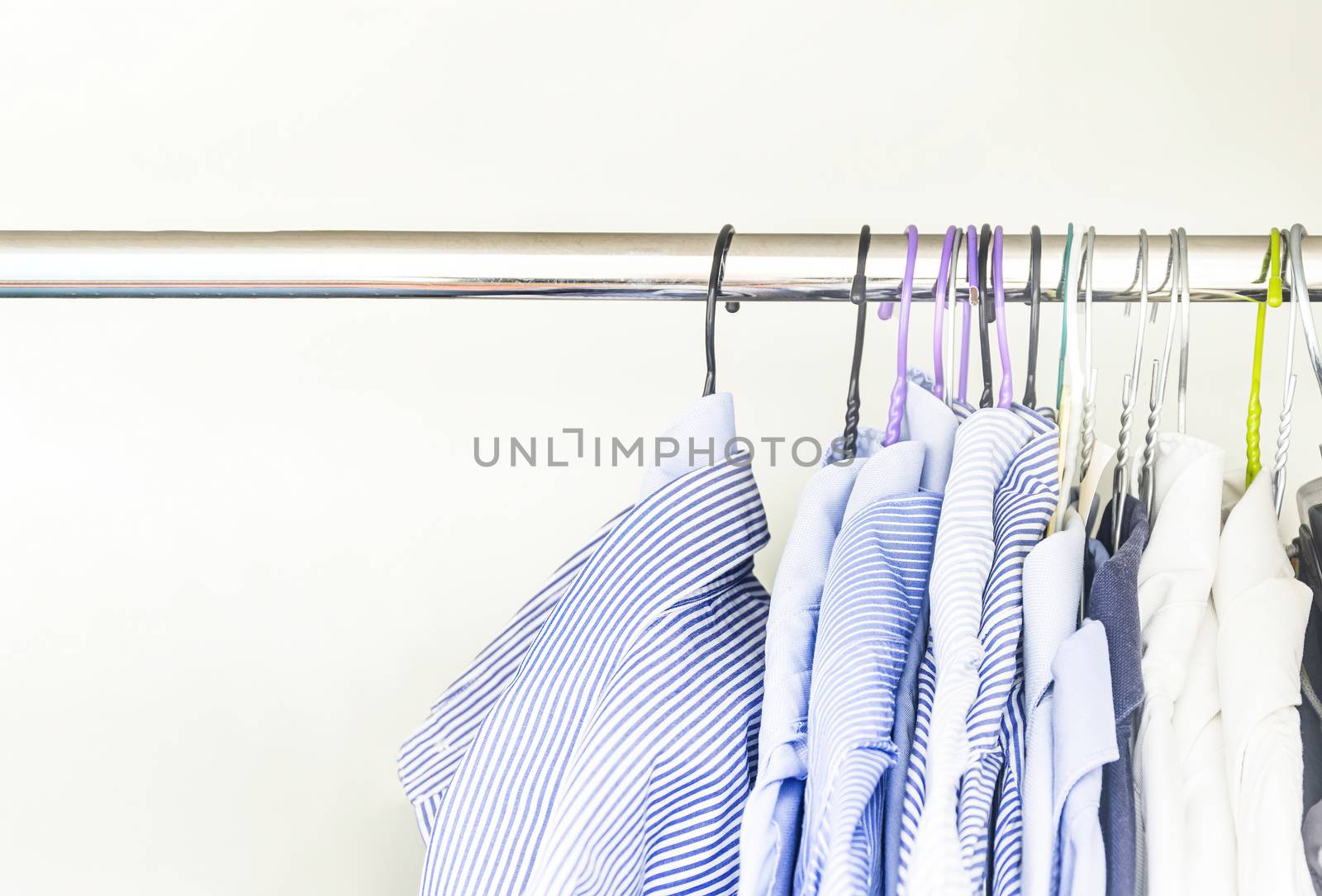 A group of men's shirts of various colors hung with hangers inside a wardrobe. Fashion and clothes.