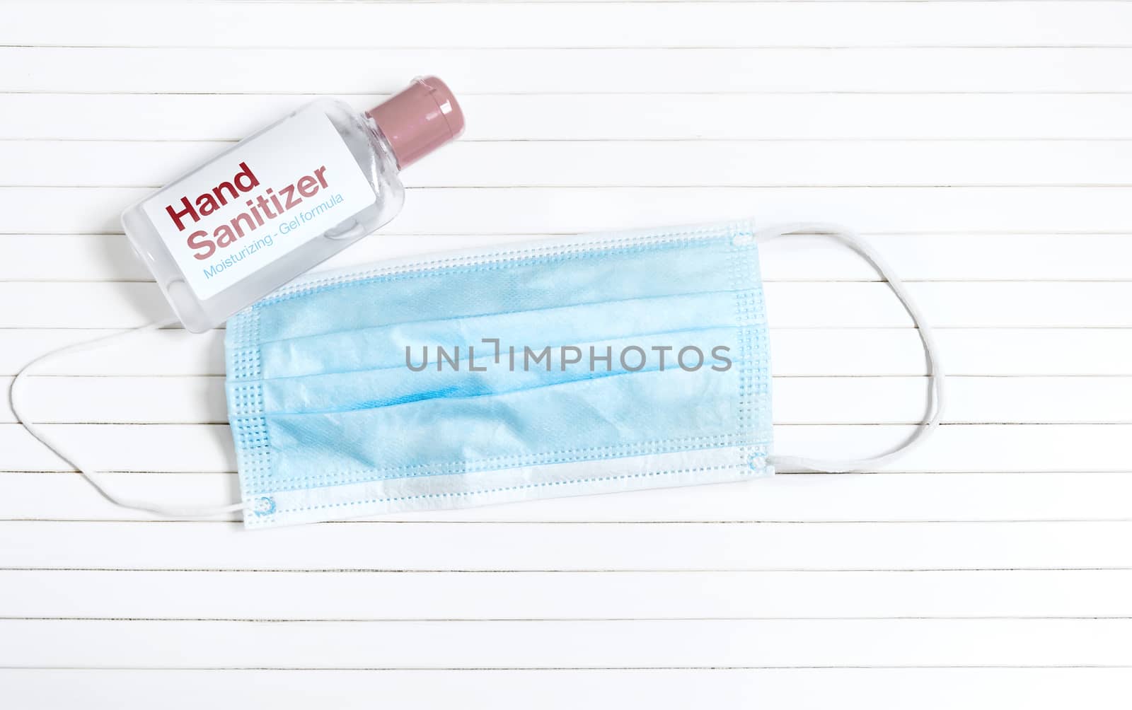 a plastic bottle containing hand sanitizing gel next to a celestial surgical mask on a white striped background. Prevention and sanitation