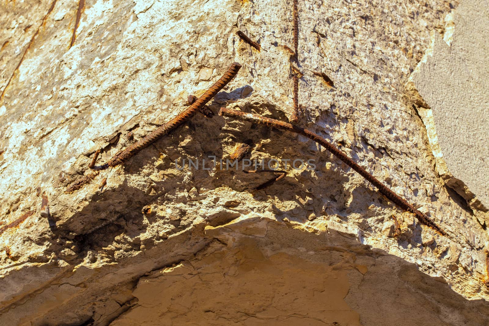 Old damaged reinforced concrete corner under direct orange sunlight with bare rusted steel skeleton. Selective focus technique.