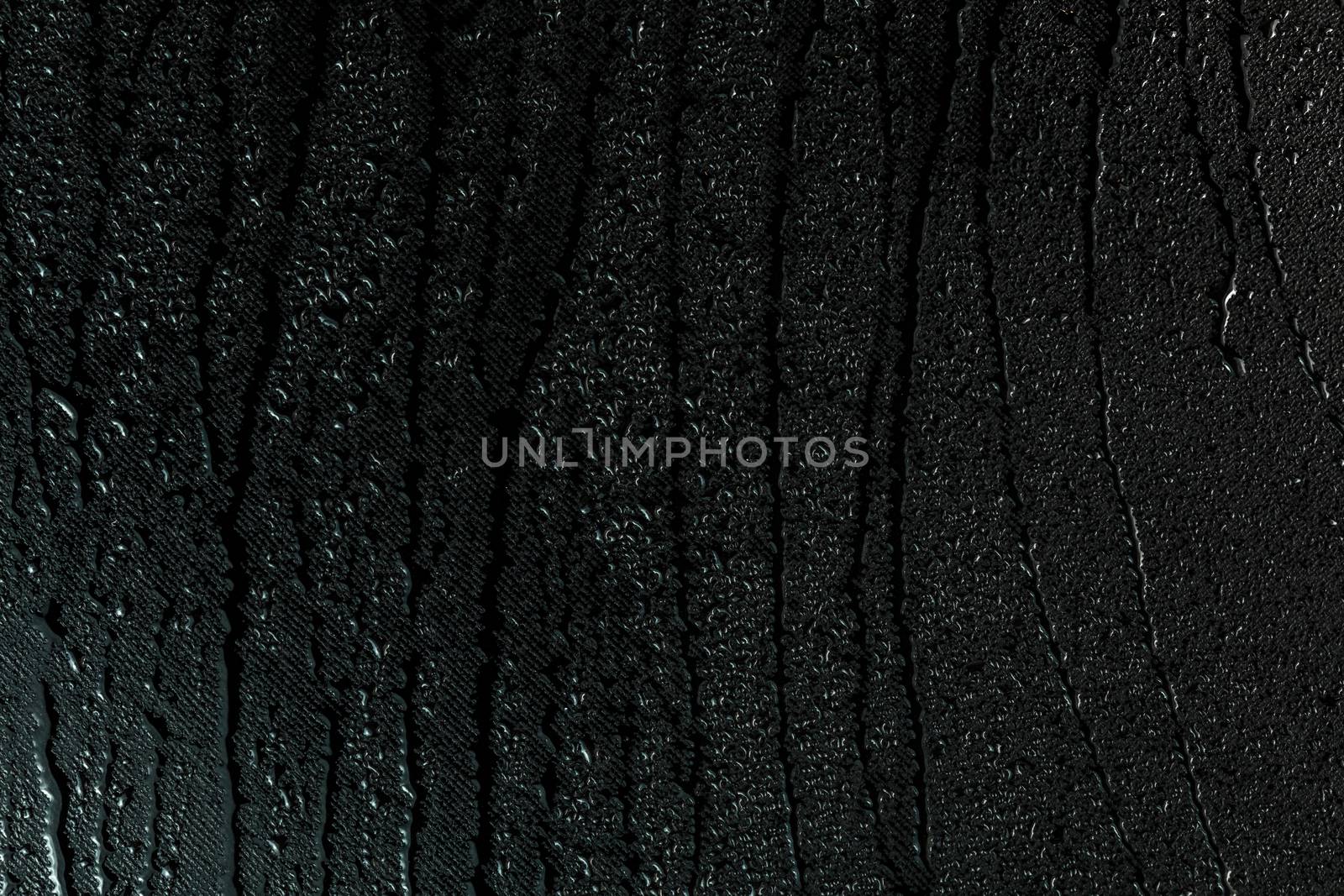 water drops on flat black rubber surface dark macro background with long smudges