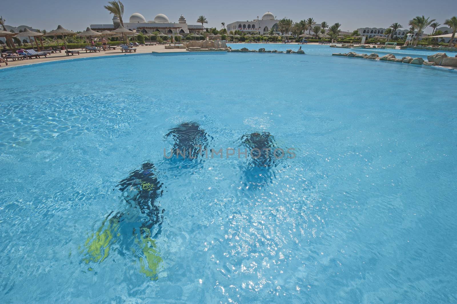 Three scuba divers training underwater in luxury tropical hotel resort swimming pool