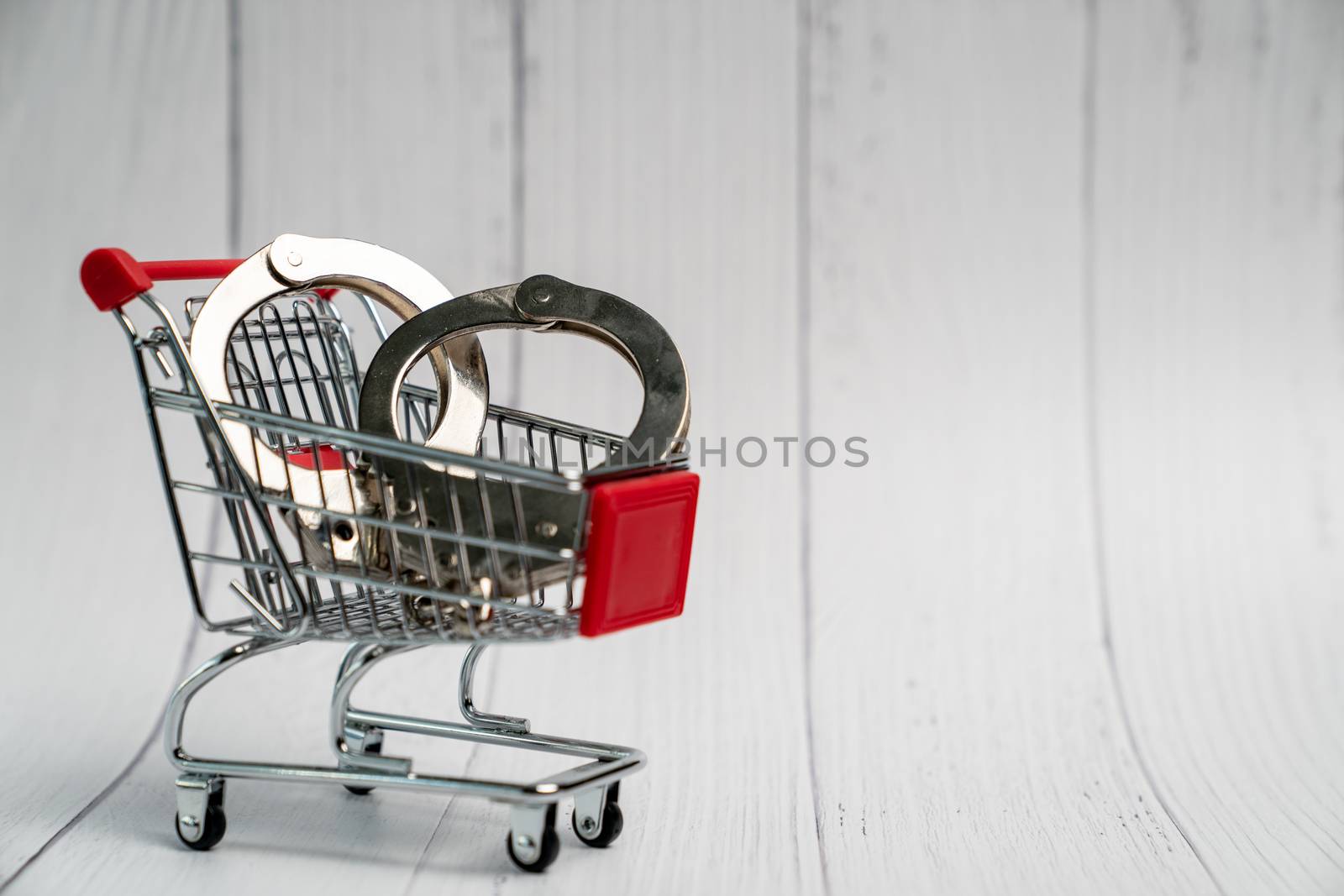 Tiny shopping cart with handcuff on on white wooden background. by sirawit99