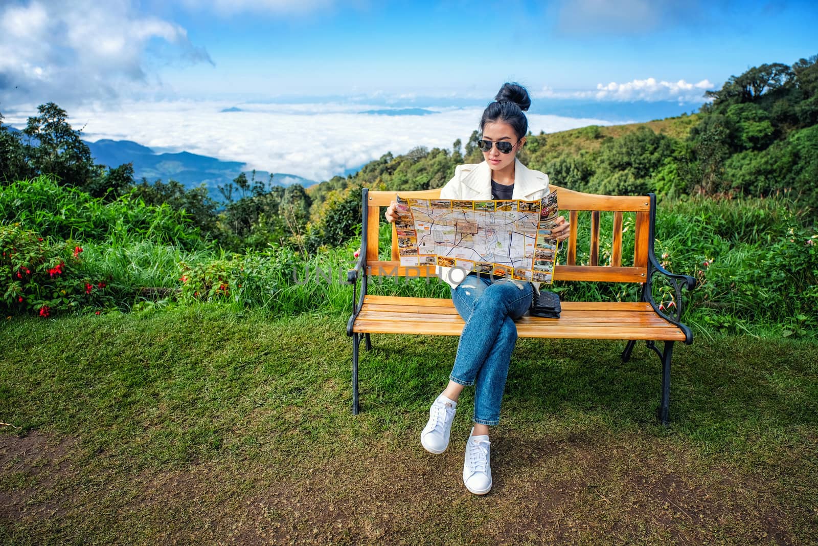 Happy woman reading a map siting on wooden chair on top of mount by Surasak