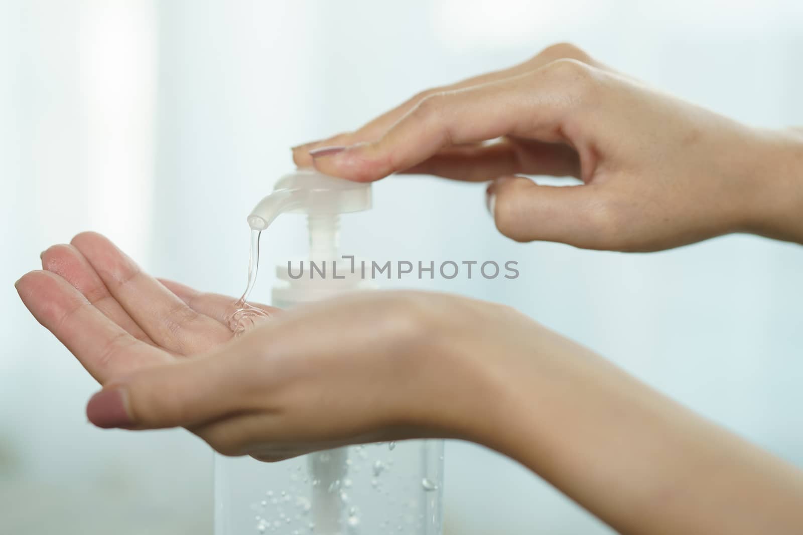 Female hands using wash hand sanitizer gel pump dispenser. Clear sanitizer in pump bottle, for killing germs, bacteria and virus.