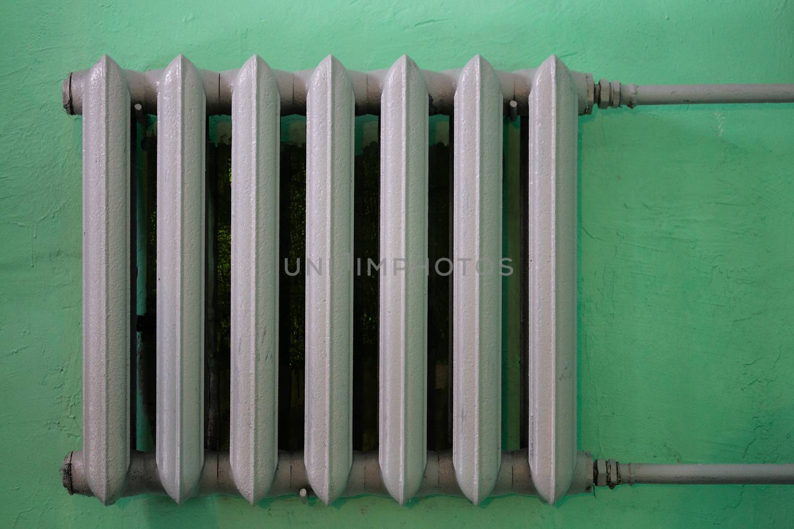 gray painted cast iron water radiator on green wall.