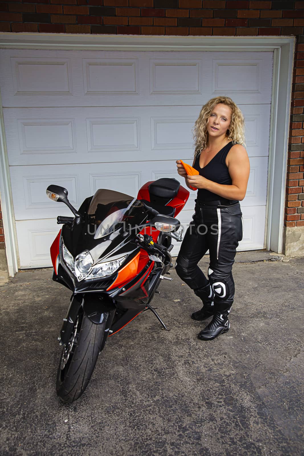 twenty something blond hair woman, about to clean a sport motocycle, in front a of garage door