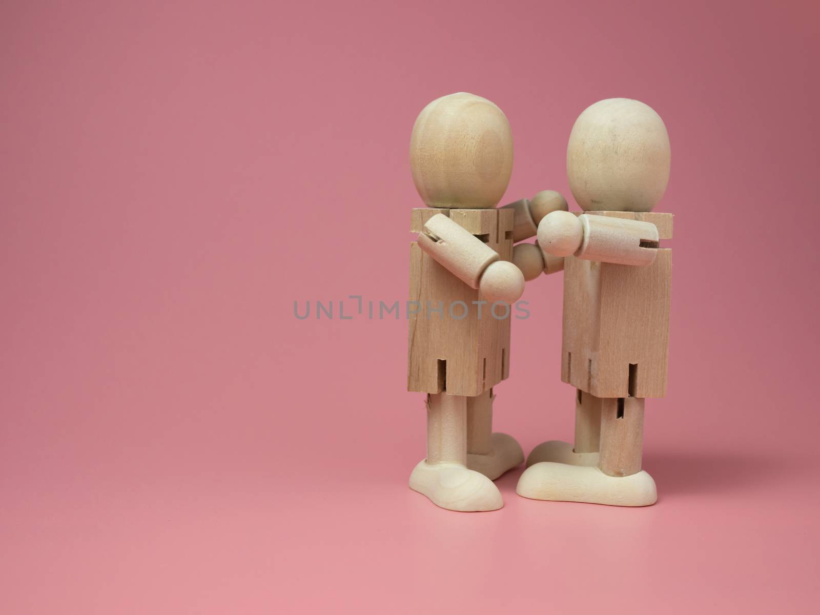 2 wooden dolls hugging each other on a pink background.
Concept of social contact from wooden dolls.