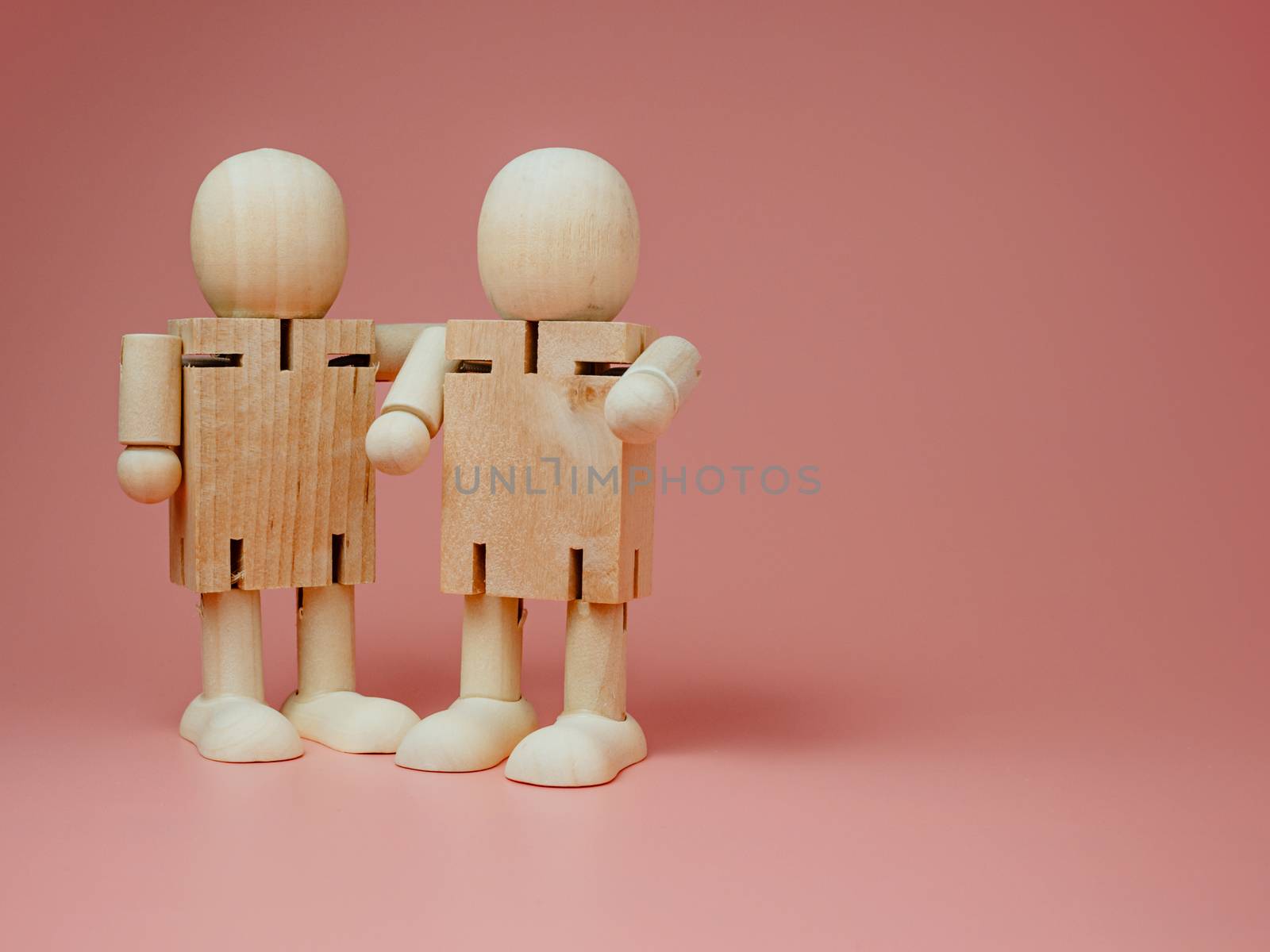 2 wooden dolls hugging each other on a pink background. Concept by Unimages2527