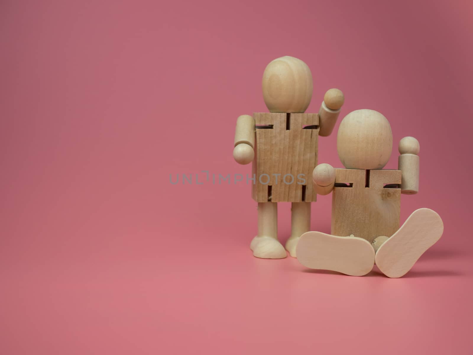 2 wooden dolls sitting and standing Talk gestures On the pink background. Concept of social contact from wood dolls. by Unimages2527