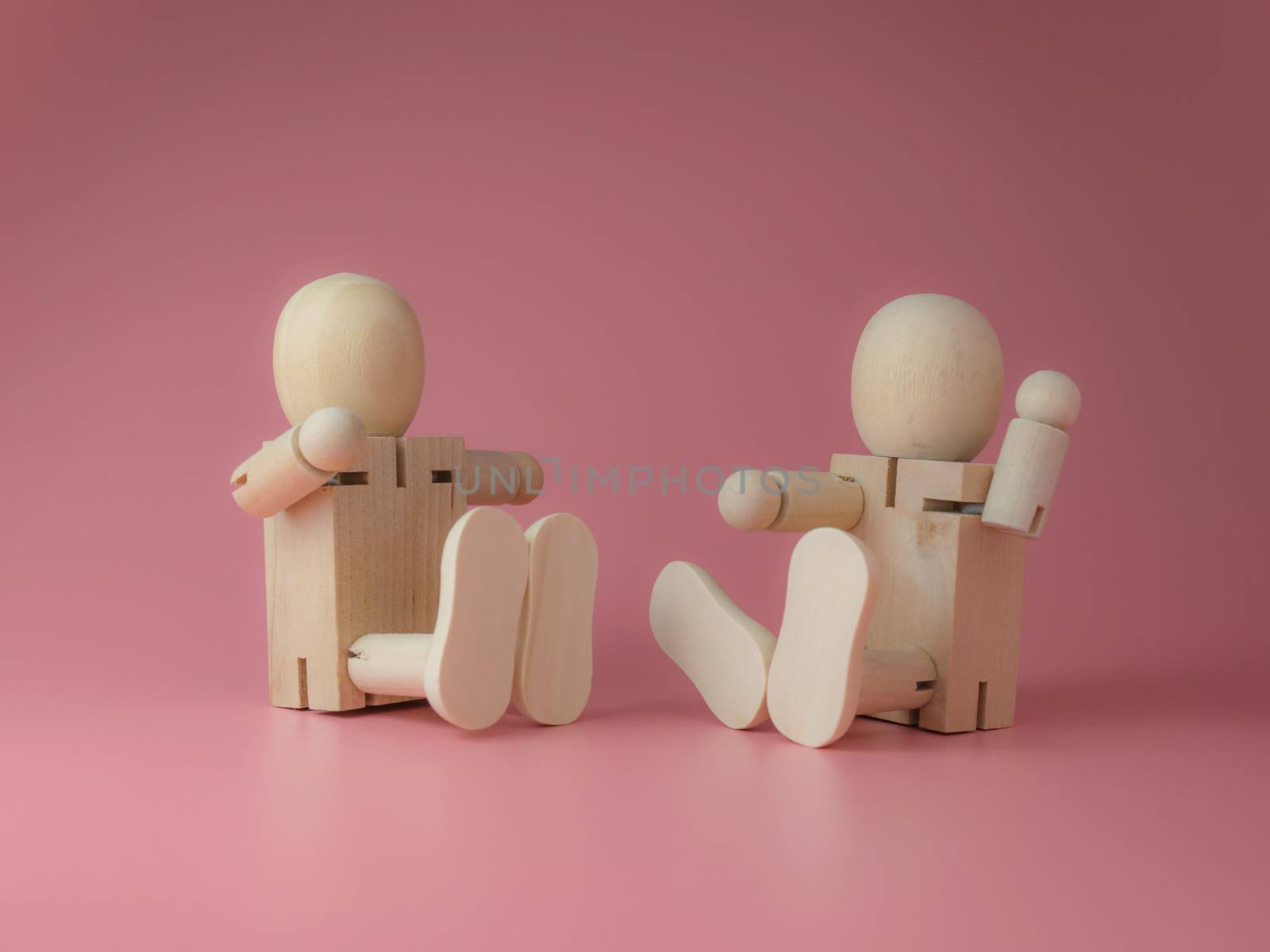 2 Wooden doll sitting and talking gestures on a pink background.
Concept of social contact from wooden dolls.
