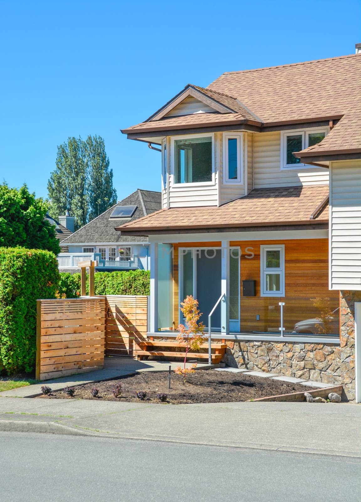 Main entrance of brand new family house in suburban. House for sale on blue sky background. Residential house with porch over the entrance door and concrete pathway over the front yard.