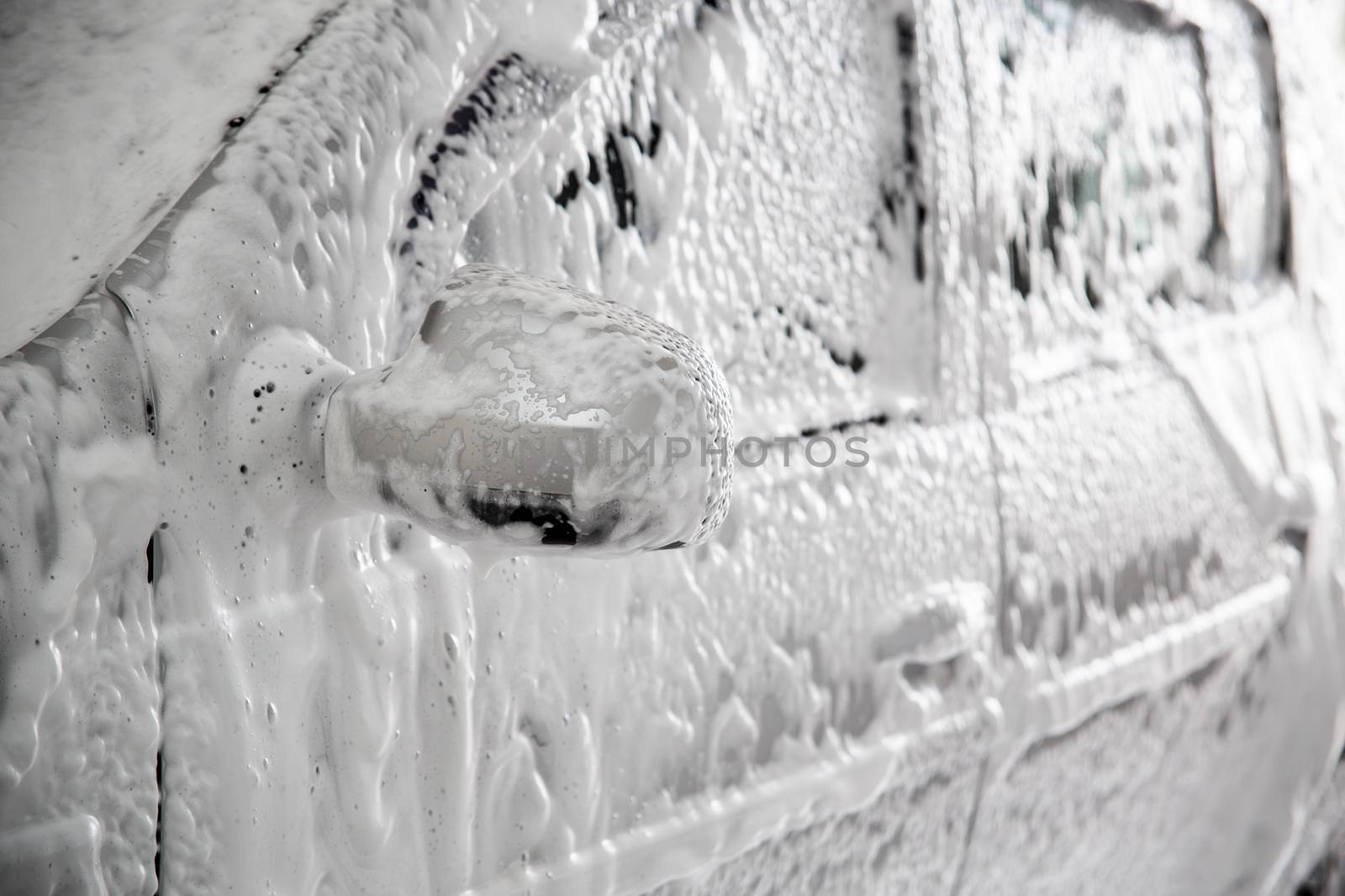 Closeup view of motor car with solid layer of soap sud during car wash. Selective focus with shallow depth of field,