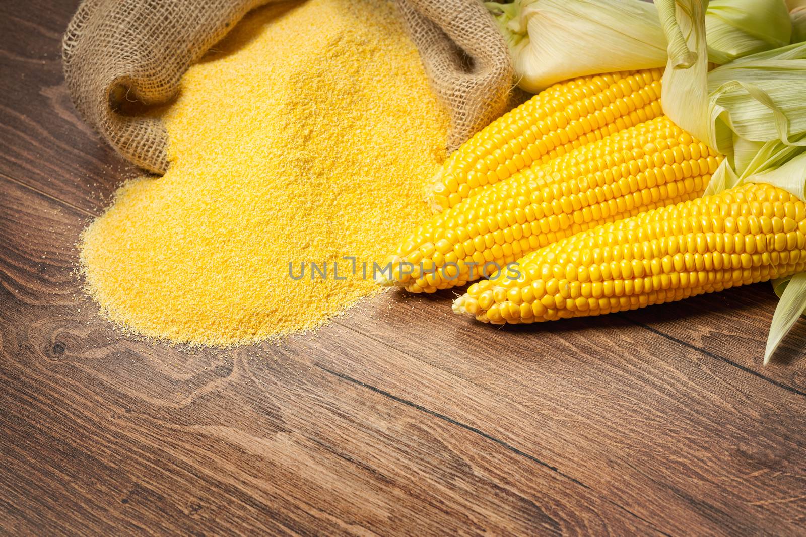 Ripe young sweet corn cob,on left stack cornmeal on wooden background, copy space.Gluten free food concept