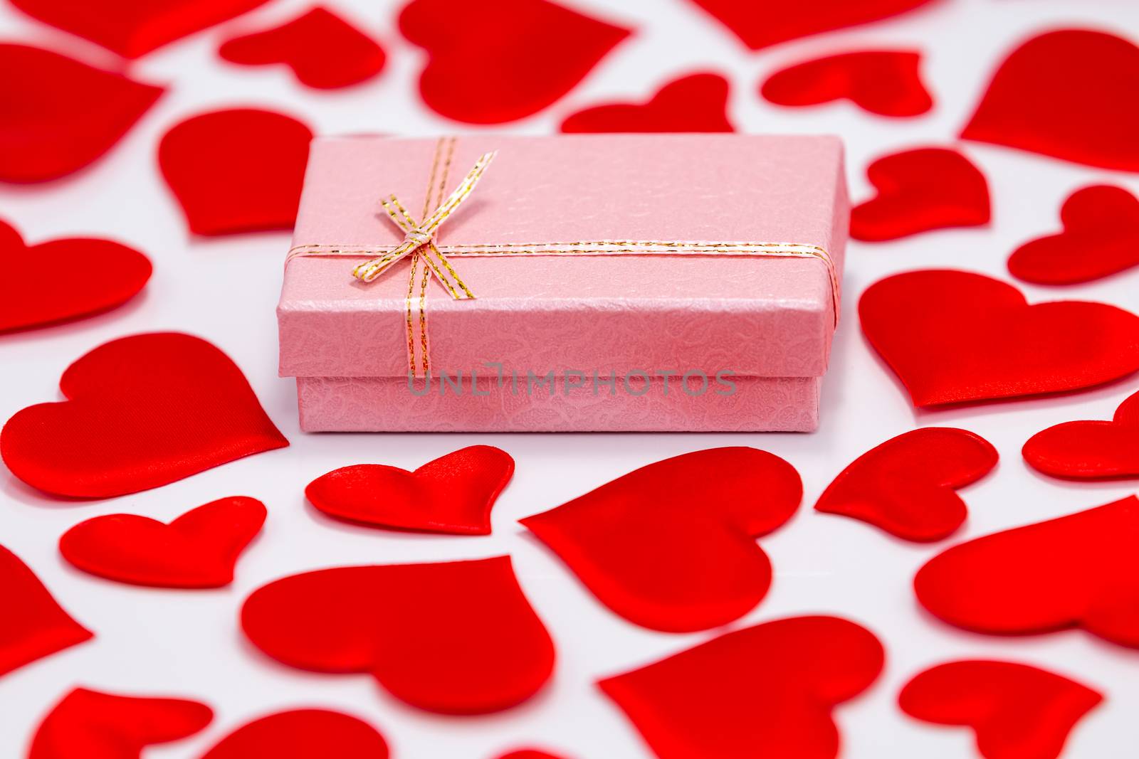 Top View of a Pink Gift Box Surrounded by Scattered Hearts on White Background. St. Valentines Day Concept