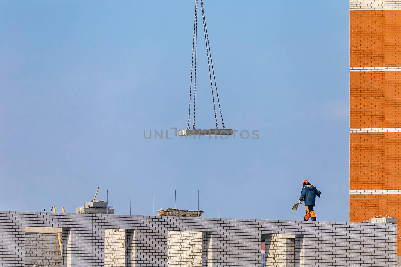 View of Construction Site. Worker Walking with a Shovel. Background With Blue Sky, Unfinished Apartment Building, Crane Chains