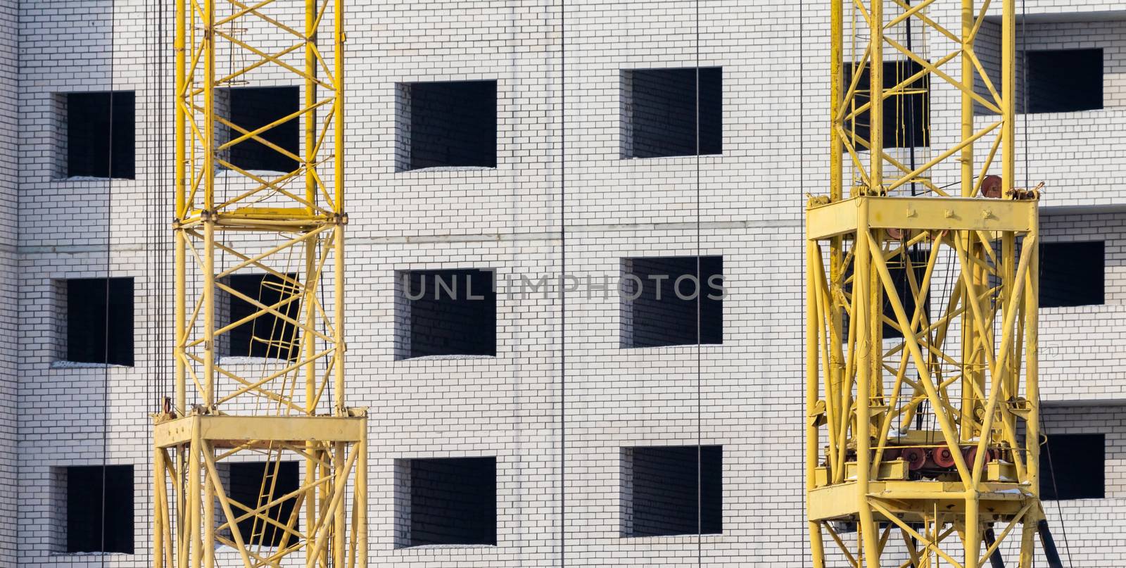 Construction site. Unfinished apartment building made of white bricks. Special yellow industrial construction cranes. Empty windows and balconies.