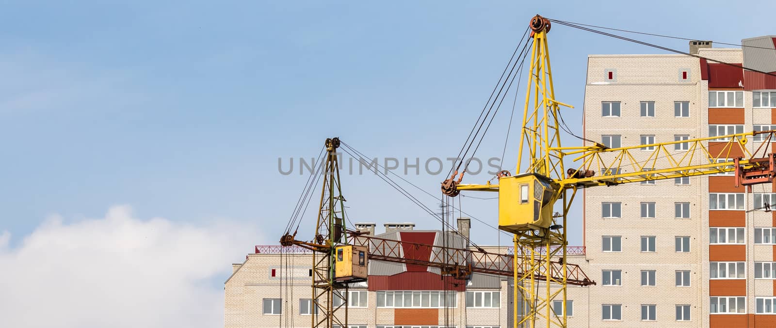 Construction site. Unfinished apartment buildings. Huge industrial cranes in the middle. Blue sky background.