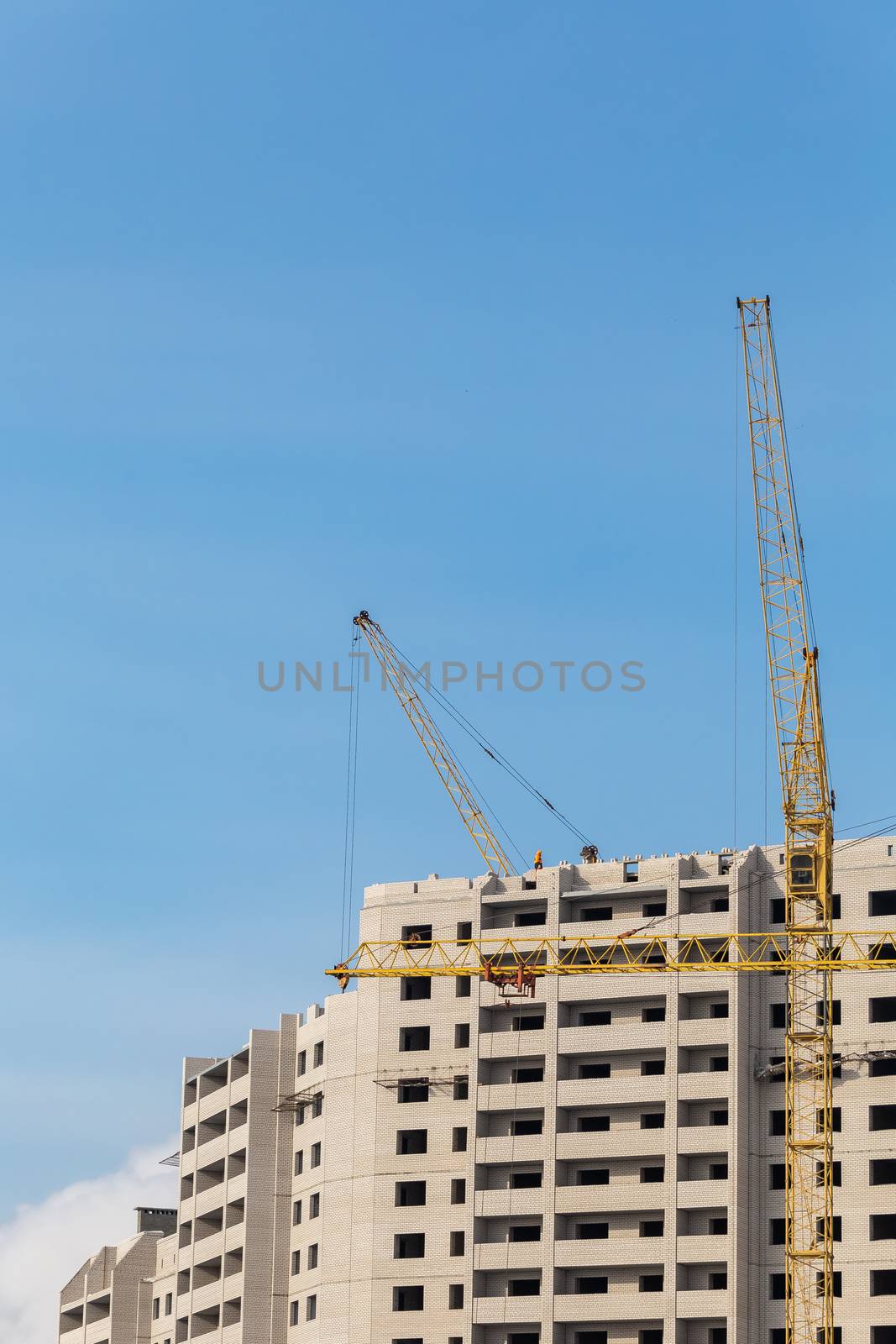 Construction site. Unfinished apartment buildings. Construction worker laying bricks on top. Special industrial cranes. Blue sky background