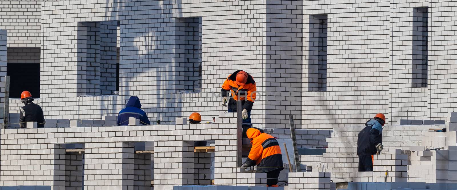 Construction site. Unfinished apartment building. Construction workers dressed in special clothing laying bricks.