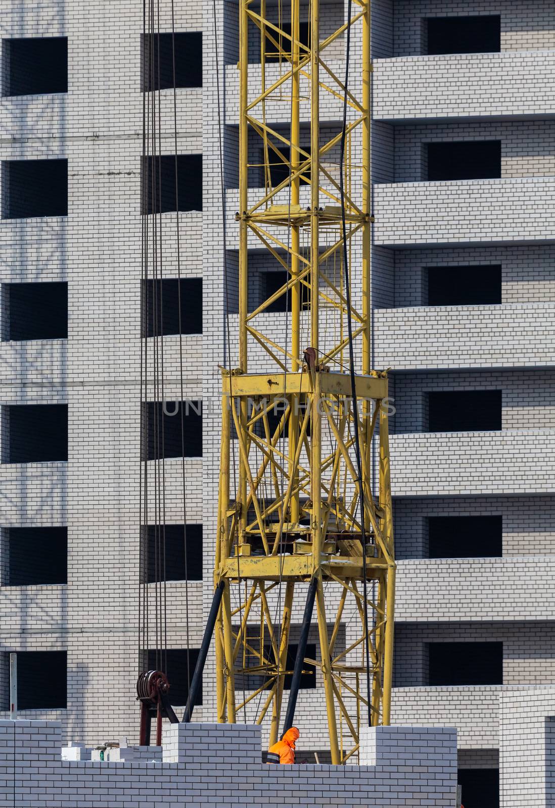 Construction site. Unfinished apartment buildings. Construction workers laying bricks. Special cranes in the middle. Blue sky background.