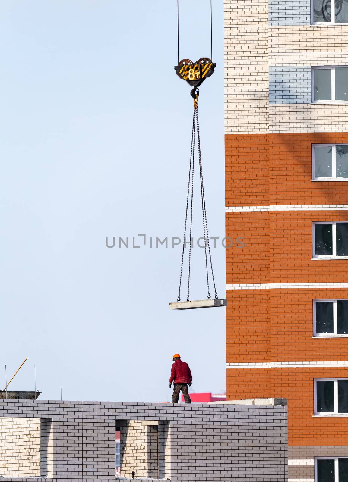Construction site in Russia. Concrete panel being lifted, worker, crane by DamantisZ