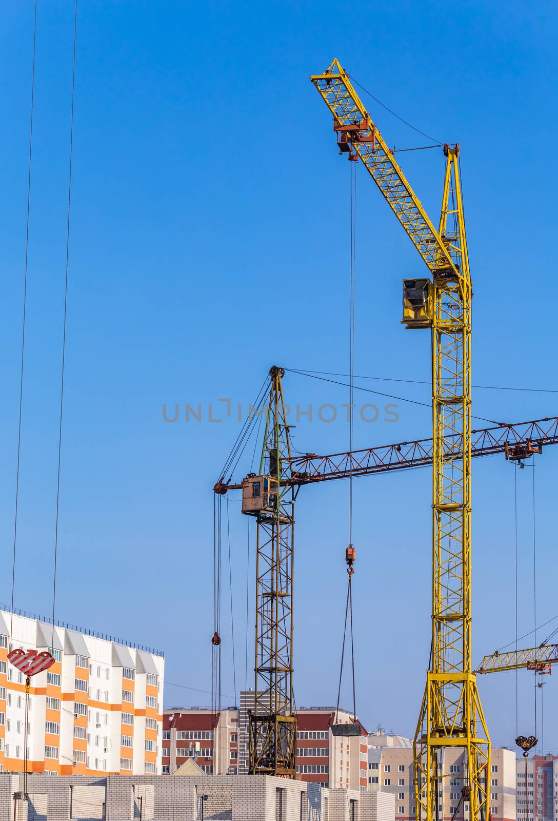 Construction site. Unfinished apartment buildings. Special industrial cranes in the middle. Blue sky background.