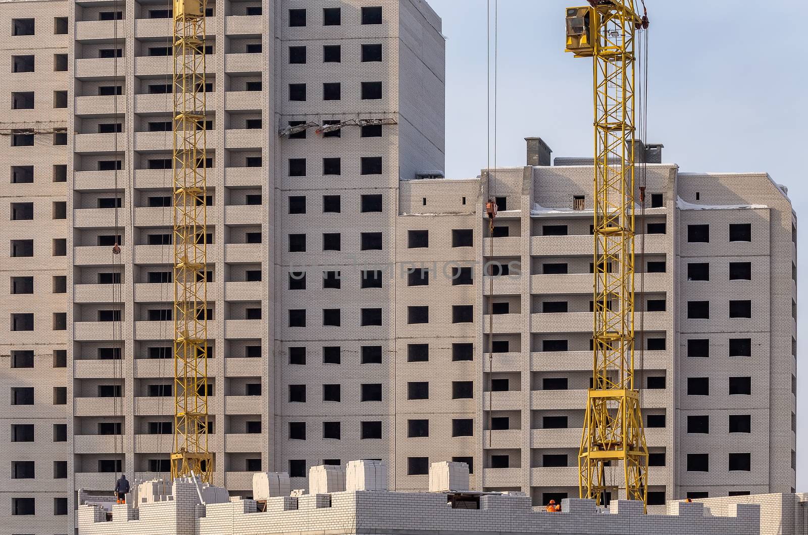 Construction site. Unfinished apartment buildings. Construction workers laying bricks. Special cranes in the middle