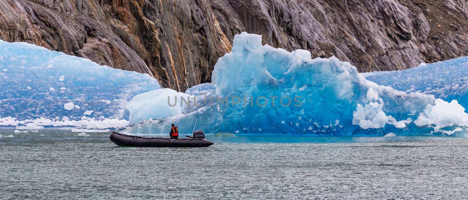 Single tourist sailing in a speed boat by a huge iceberg floating in a fjord. Alaska, USA