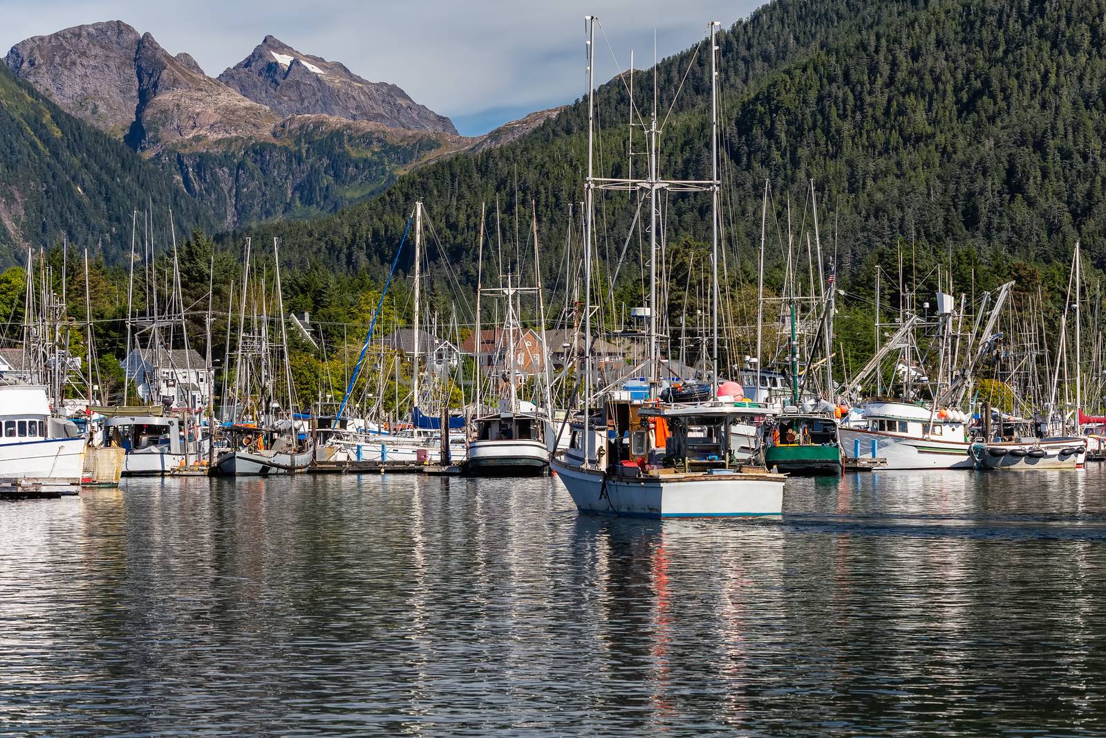 Fishing boat sailing in marina and is about to dock. Marina full of other fishing boats. Gorgeous mountains and forest in the background. Sitka, AK