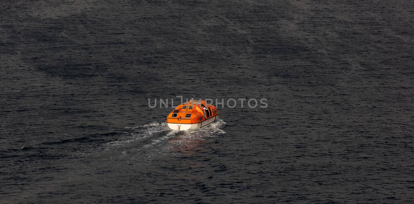 View of a single orange life boat with some seamen inside sailing at sea. Caribbean sea.