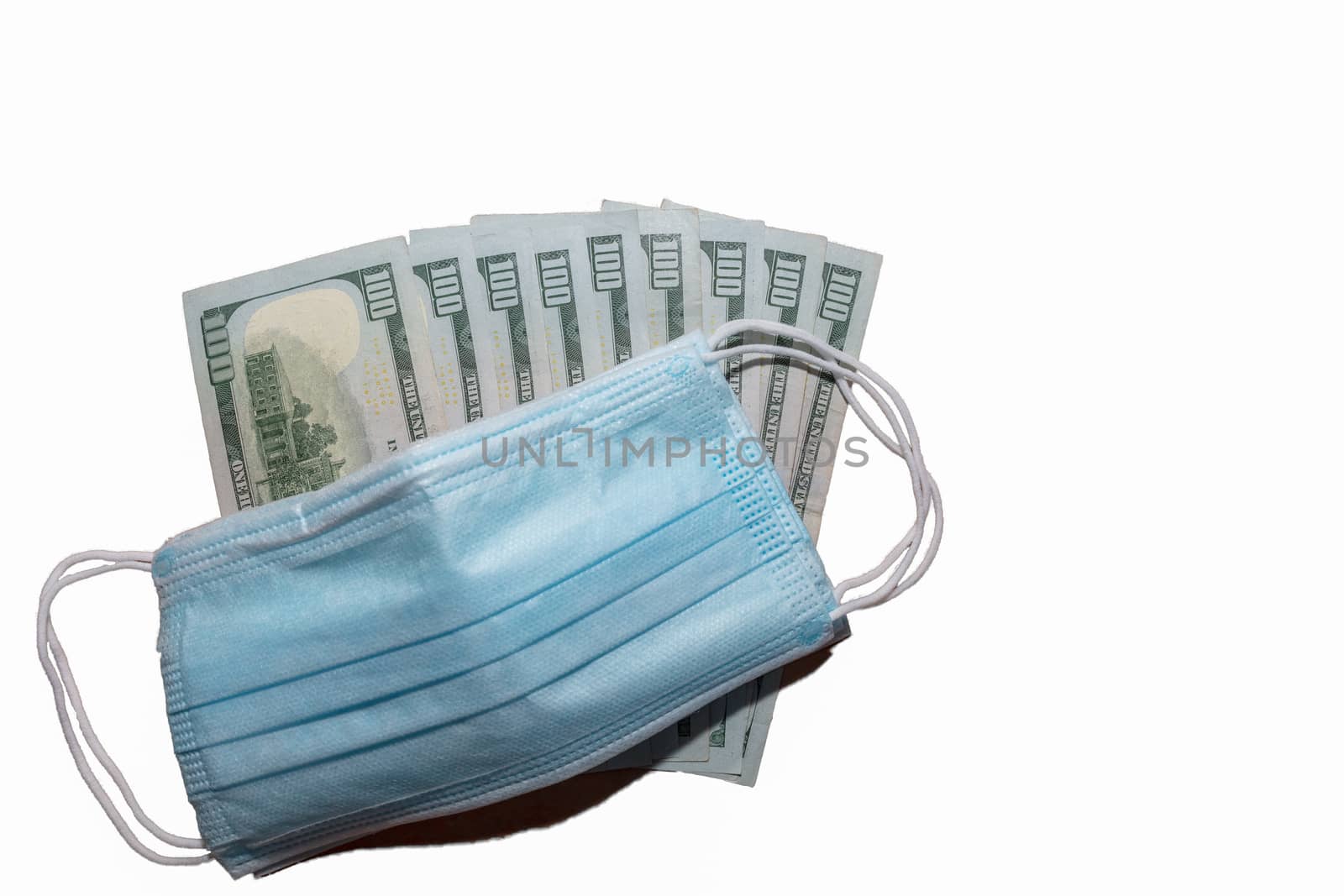Facial protective surgical masks on top of a few hundred dollar bills. Isolated. White background. Expensive protection against viruses and bacteria.
