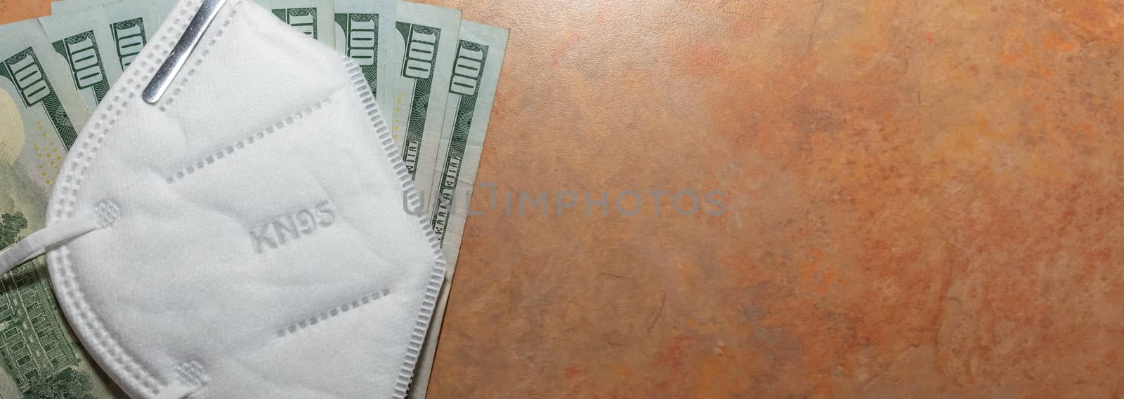 Part of facial protective mask KN95 on top of a few hundred dollar bills. Marble table background. Expensive protection against viruses and bacteria.