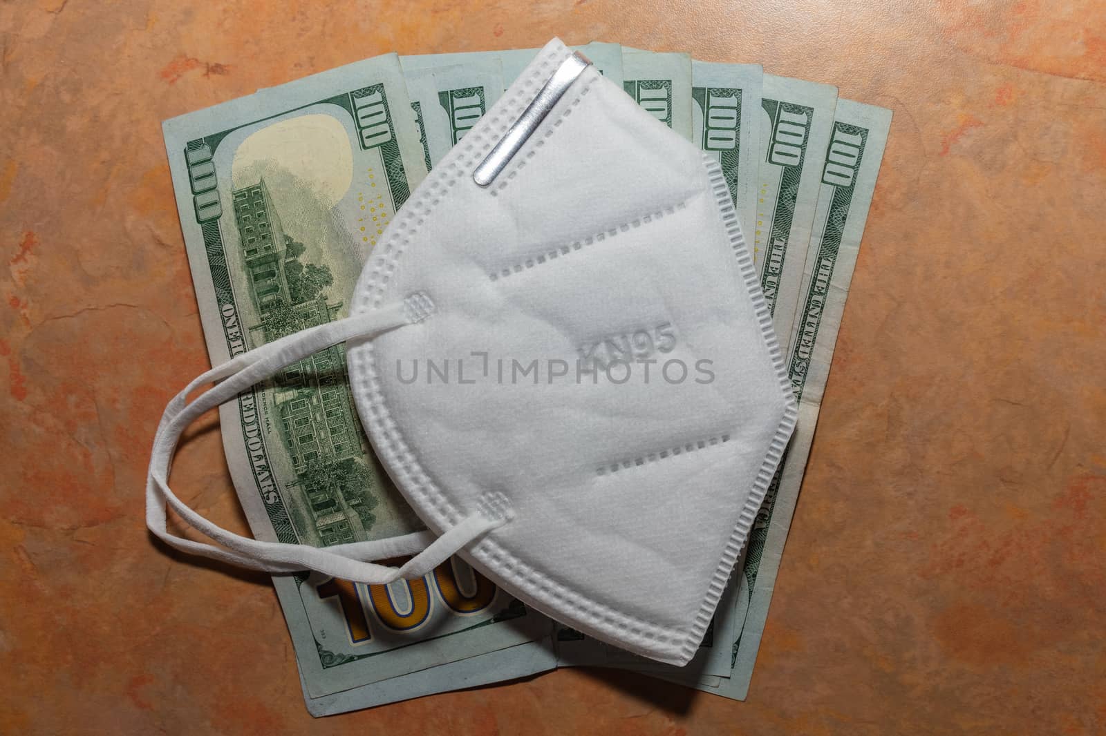 Facial protective mask KN95 on top of a few hundred dollar bills. Marble table background. Expensive protection against viruses, bacteria, and germs.