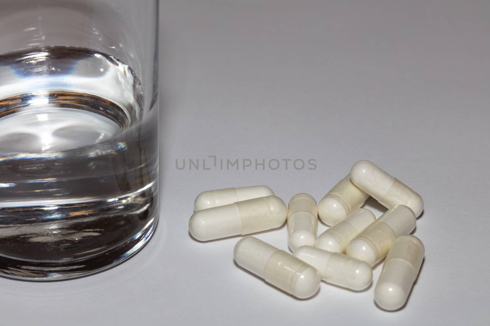 White pills and glass of water on white backdrop by DamantisZ
