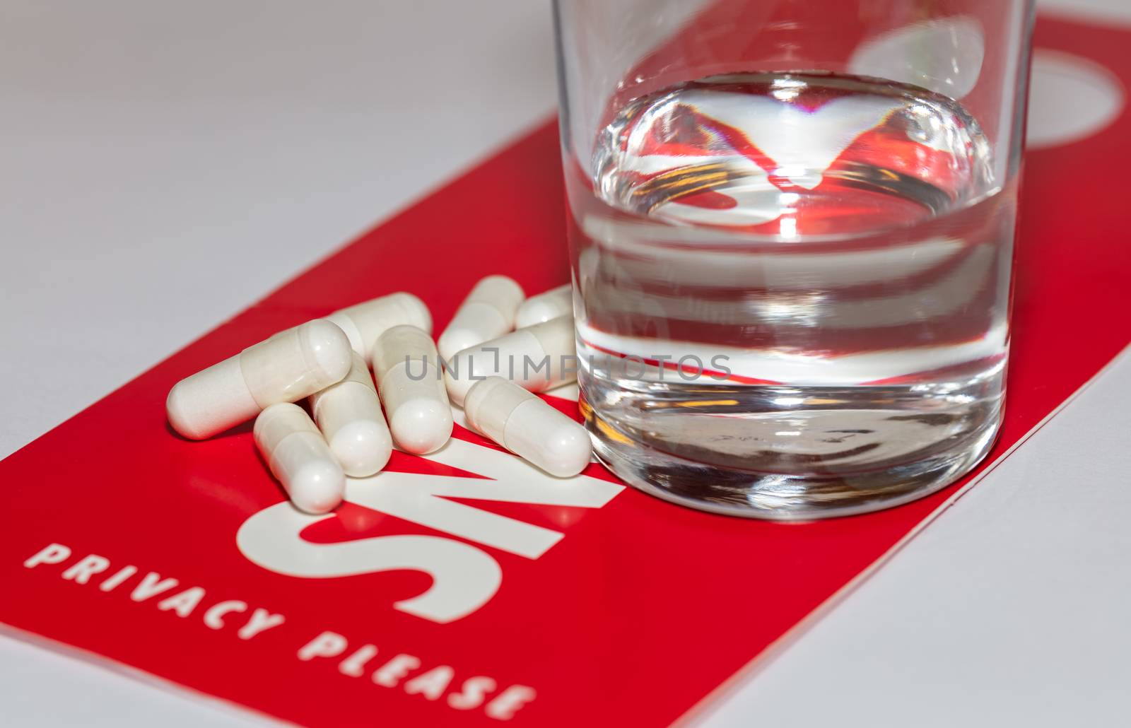 White pills and a glass of water on red privacy, snoozing sign. Snoozing sign reads Privacy please. Sign and some pills are in soft focus.