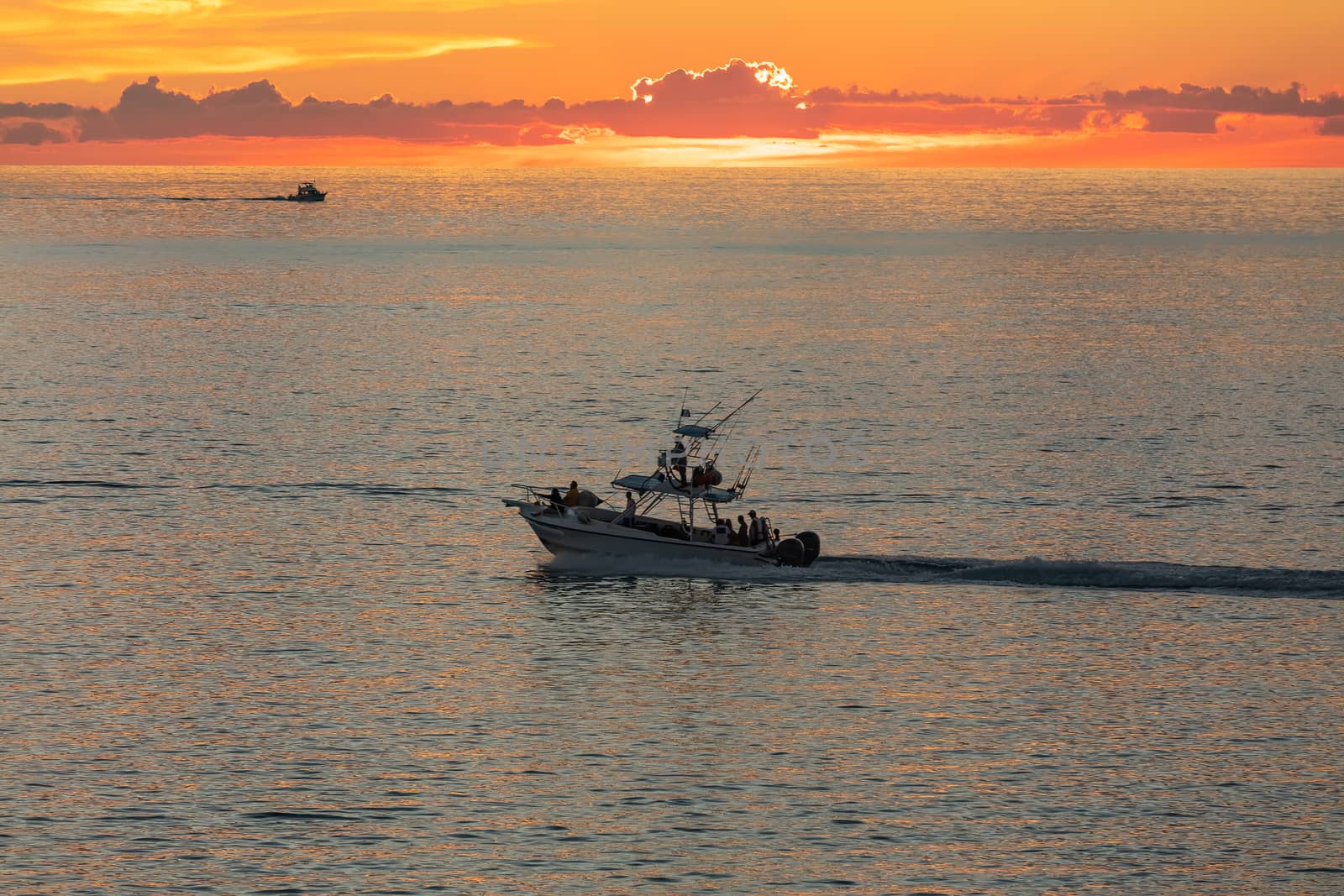 Fishing boat sailing at sunset in Mexico. Beautiful orange sky and a tiny boat silhouette in the background.