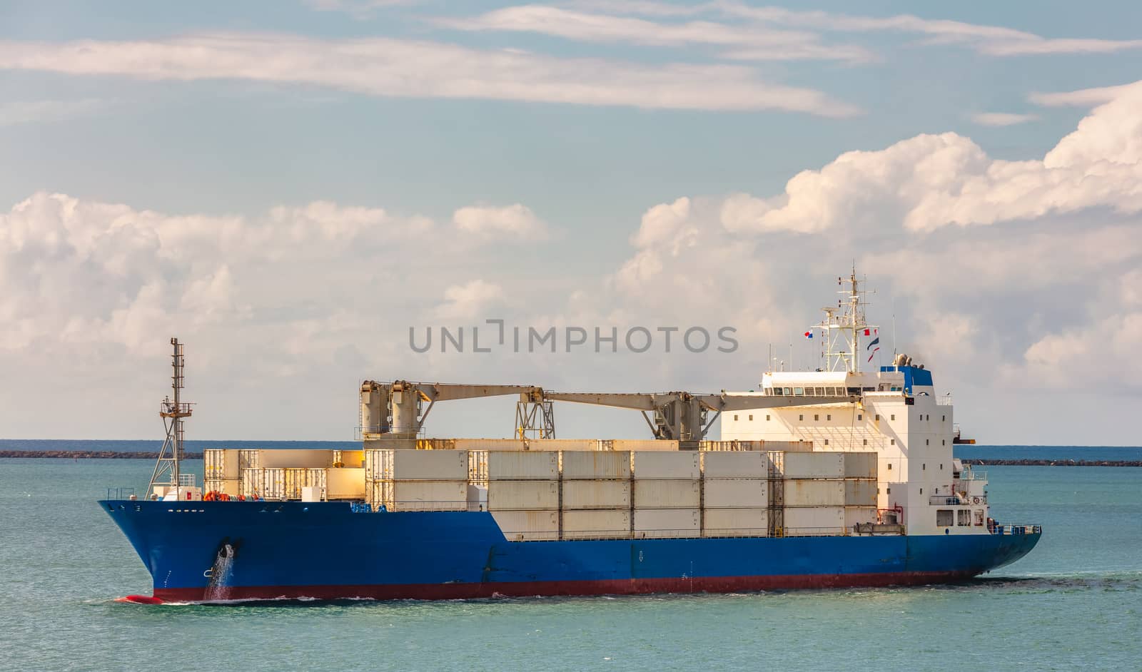 Cargo ship in Panama Canal. Various containers and cranes on deck. Shipping industry concept. Clouds and blue sky as a background