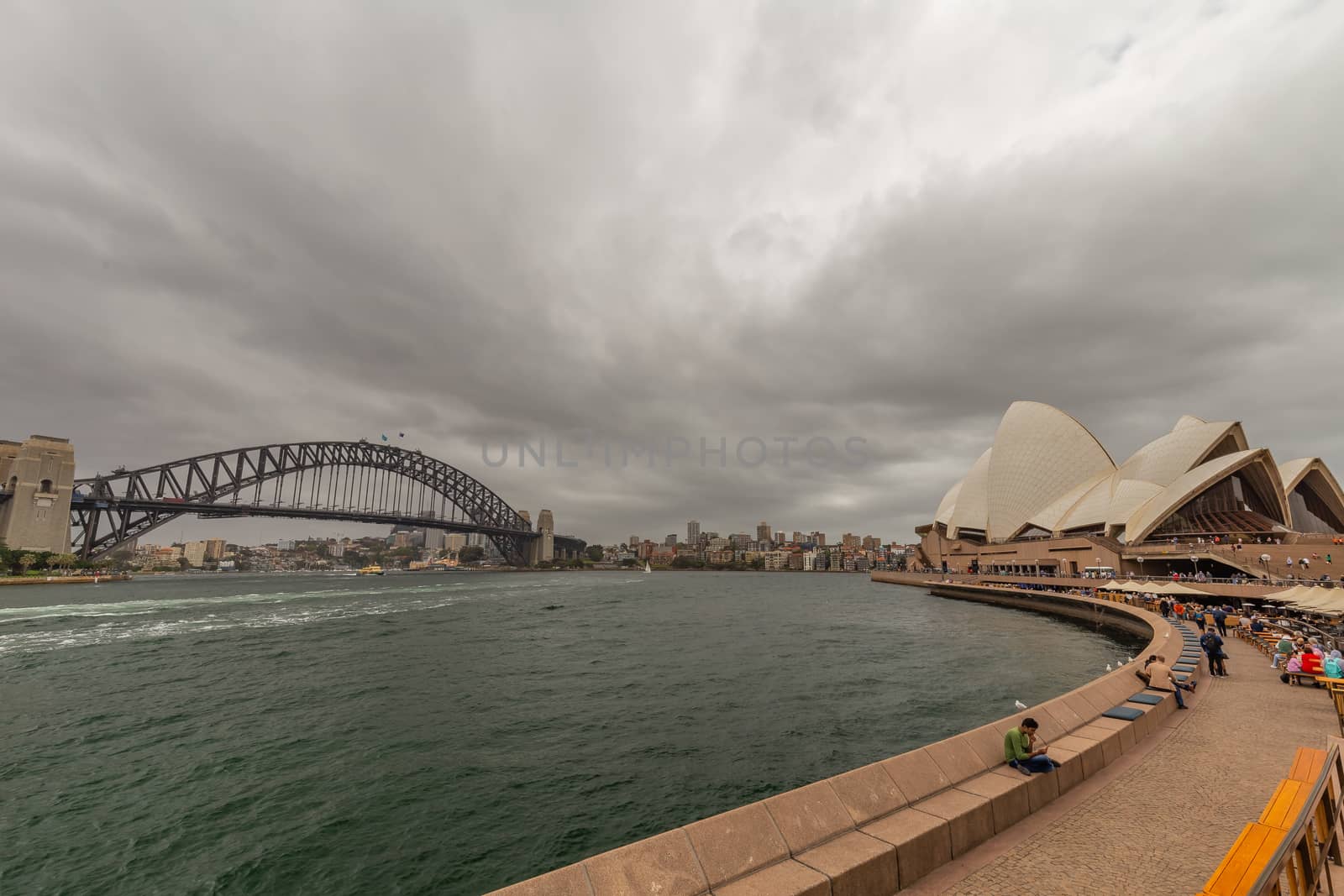 Sydney Harbor, Australia - October 23, 2018: Panoramic view of Sydney downtown, harbor bridge and opera house with boats sailing in the bay. Gloomy, cloudy sky.