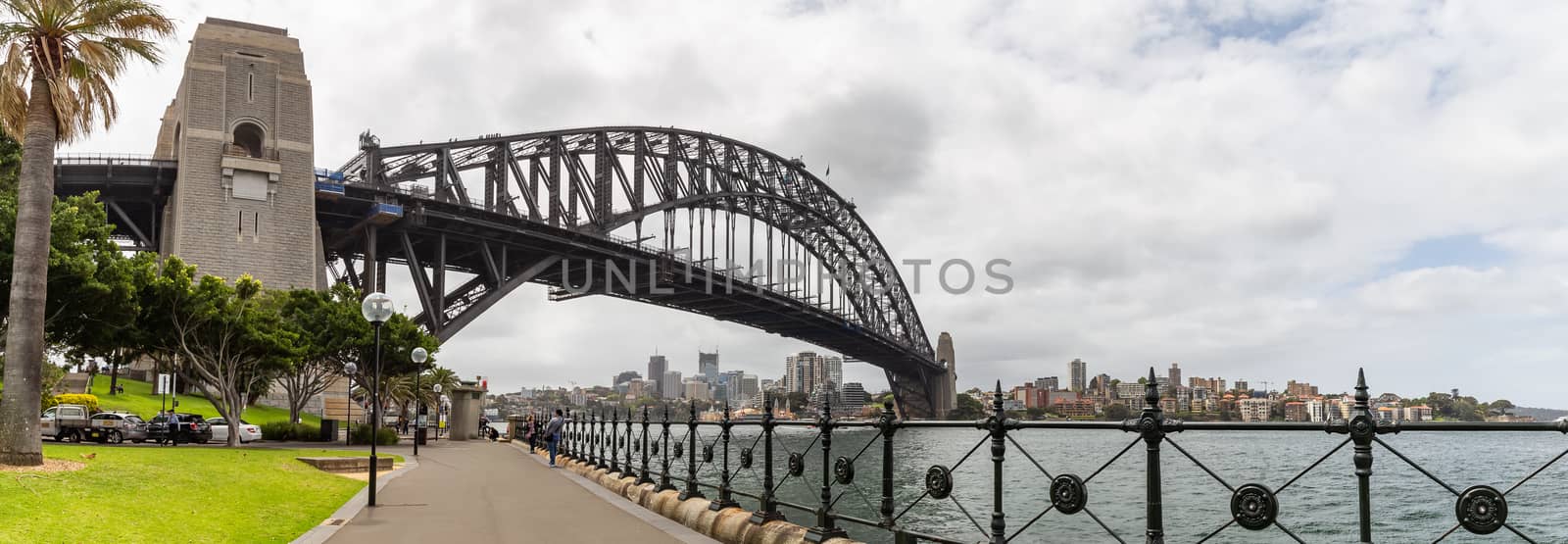 Sydney Harbor, Australia - October 23, 2018: View of Sydney harbor bridge. Cars parked next to it and tourists walking underneath it.