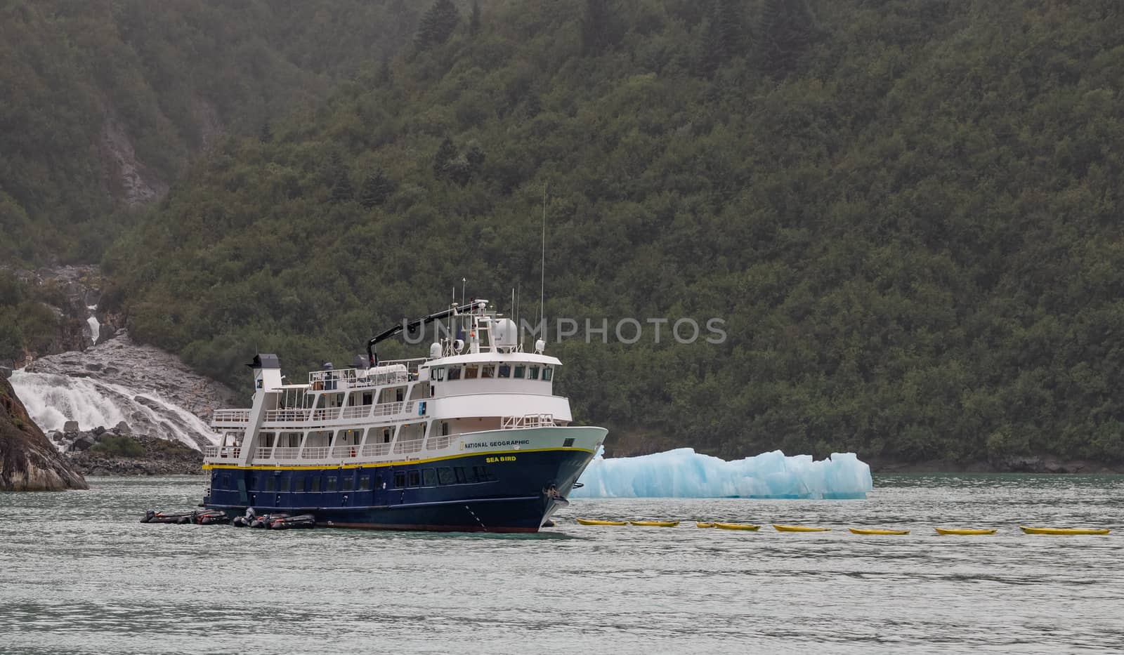 Tracy Arm Fjord, Alaska, US - August 23, 2018: National Geographic's Sea Bird vessel drifting with a mountain, a waterfall, and an iceberg behind it in Tracy Arm Fjord in Alaska, USA