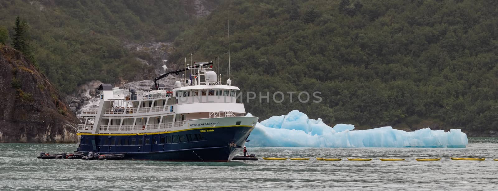 Tracy Arm Fjord, Alaska, US - August 23, 2018: National Geographic's Sea Bird vessel drifting by an iceberg with some personnel in a small boat next to it. Close view.