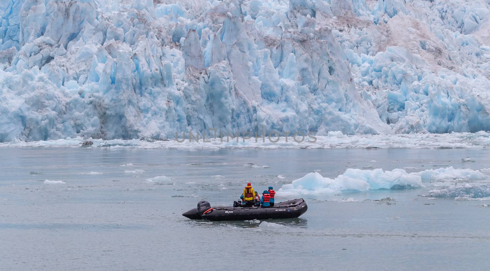 Tracy Arm Fjord, Alaska, US - August 23, 2018: Tourists and a guide in a speedboat drifting among icebergs and a glacier behind it.