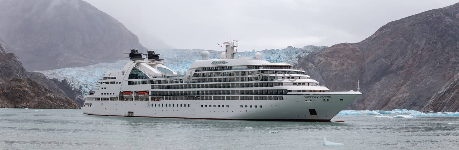 Tracy Arm Fjord, Alaska, USA - August 23, 2018: Panorama of Seabourn Sojourn cruise ship drifting with a massive glacier and mountains behind it