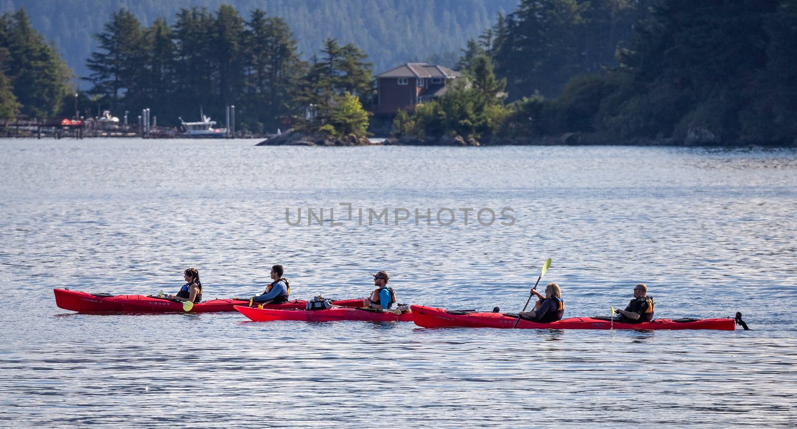 Sitka, Alaska, US - September 10, 2018: Tourists kayaking in marina. House, forest and mountains in soft focus in the background. Alaska, USA