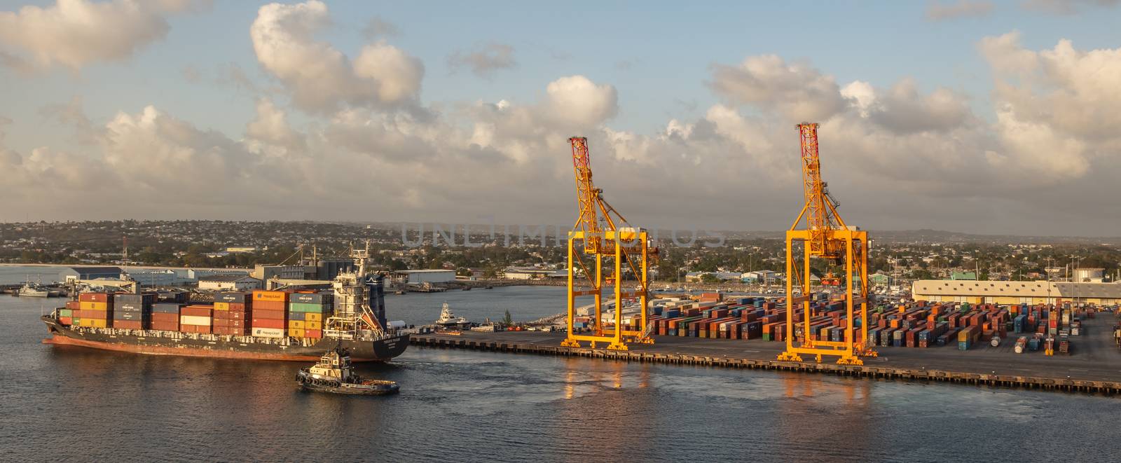 Bridgetown port, Barbados, West Indies - May 2, 2020: Bridgetown port with loading cranes and full cargo ship sailing away