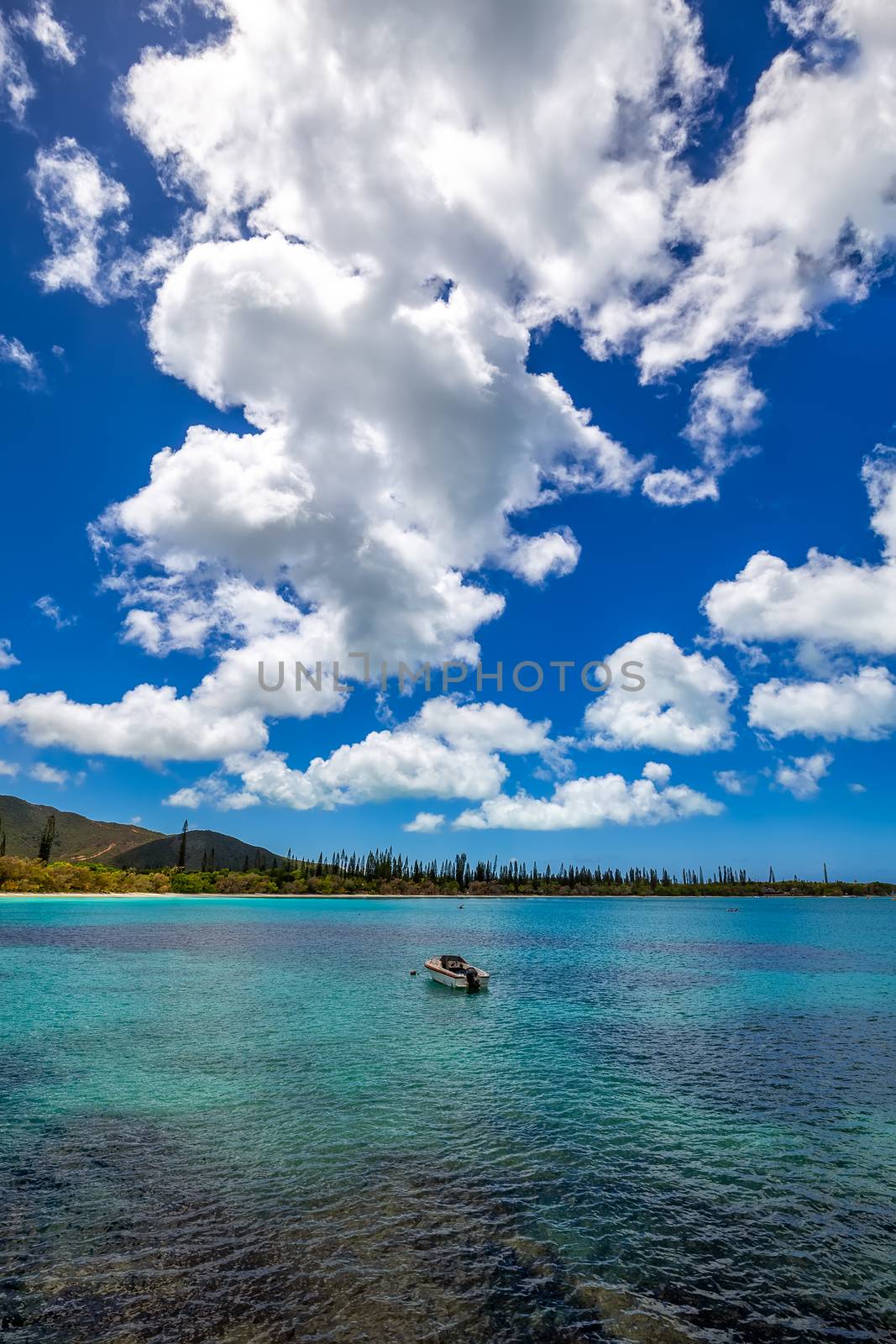 Fishing boat anchored by a tropical island with blue sky and white clouds in the background.